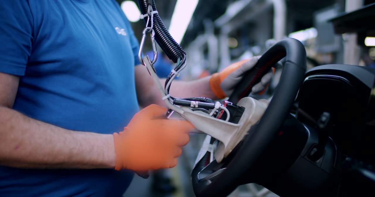 Arbeiter montiert ein Lenkrad mit freiliegender Elektronik in einer Automobilfabrik