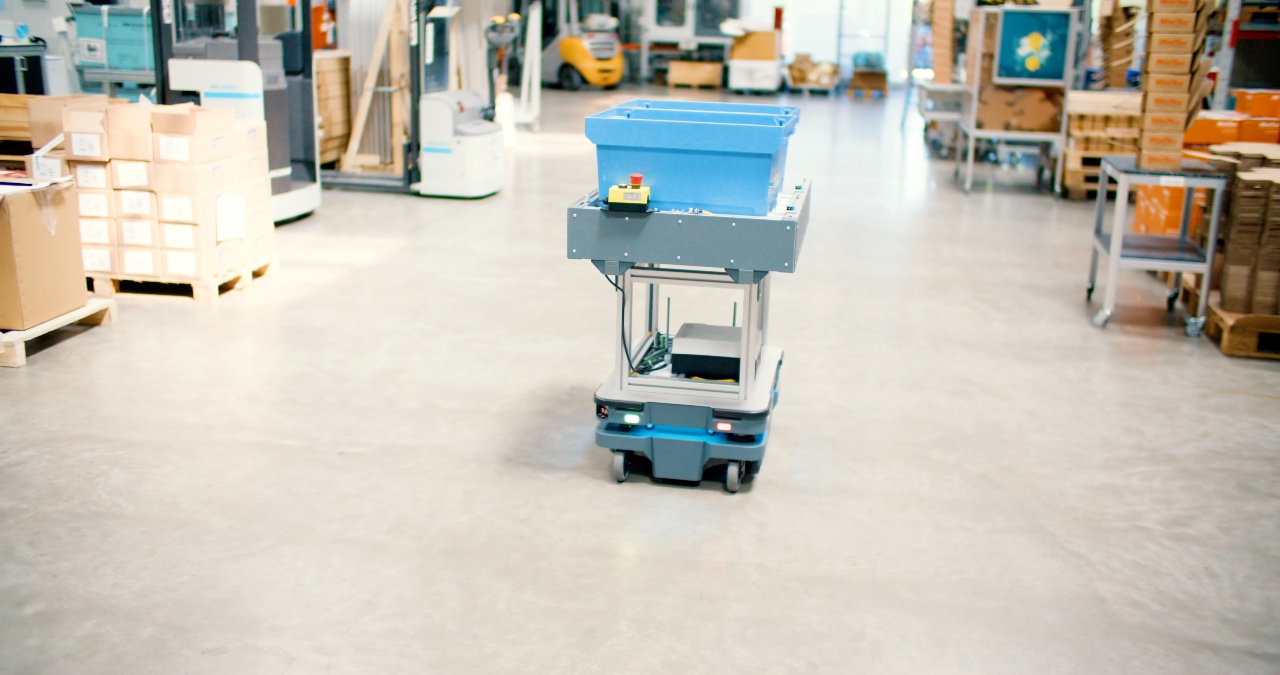 Autonomes Transportsystem mit blauer Materialbox fährt eigenständig durch ein modernes Industrielager