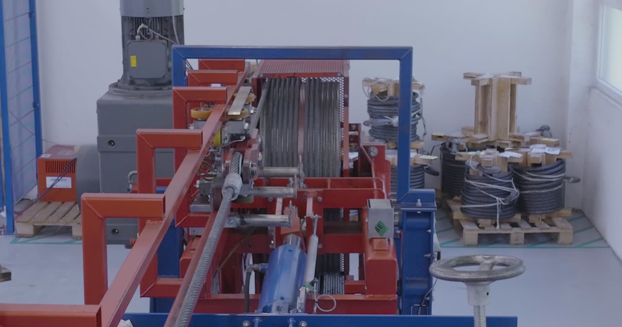 Blick auf eine industrielle Prüfanlage für Stahlseile mit gelagerten Kabelrollen im Hintergrund