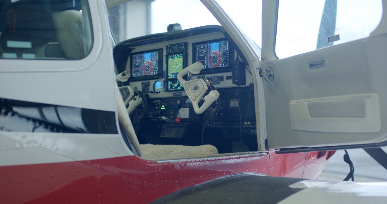 Blick durch die geöffnete Kabinentür in das moderne Cockpit eines Kleinflugzeugs mit digitalen Glascockpit-Displays