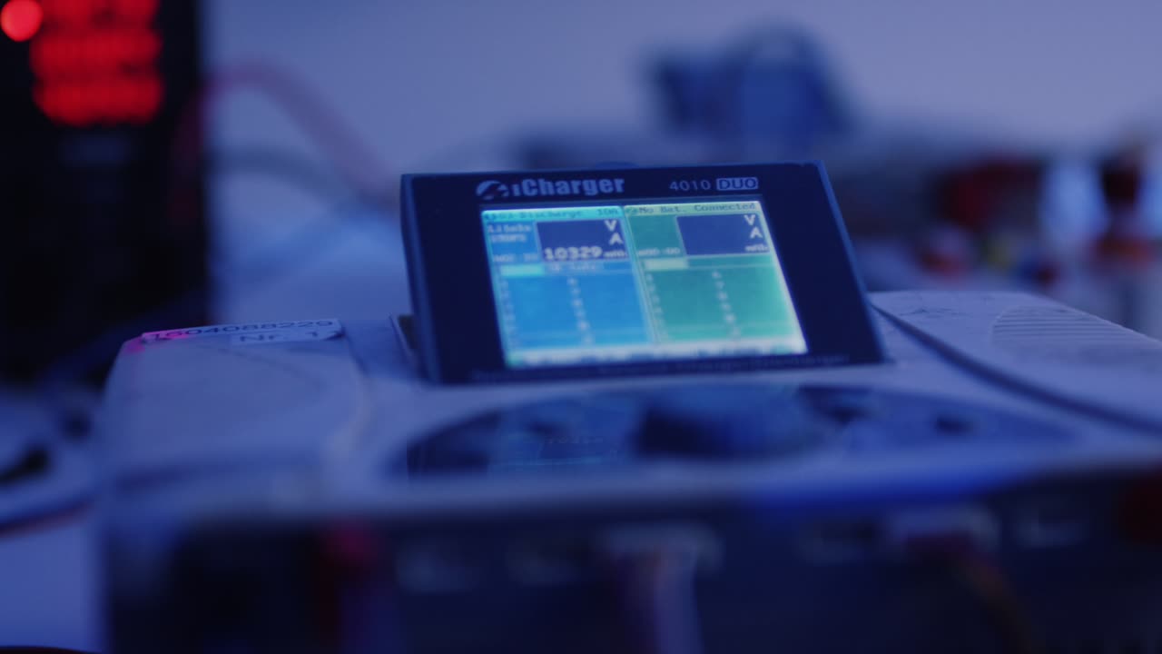 Digitales Ladegeraet mit Display und Kabelverbindungen auf einem Pruefstand bei blauem Licht