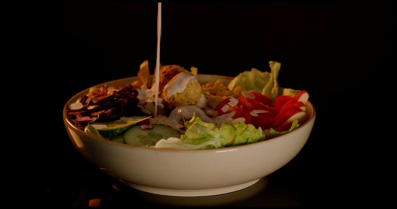 Frische Bowl mit Falafel und Gemüse wird mit Dressing verfeinert und vor schwarzem Hintergrund gedreht