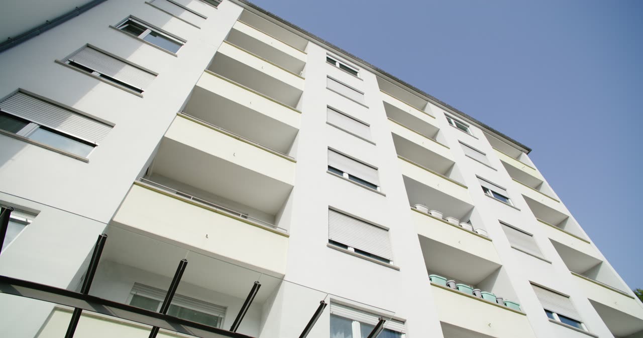Froschperspektive von einer modernen weißen Wohnhausfassade mit Balkonen gegen den blauen Himmel