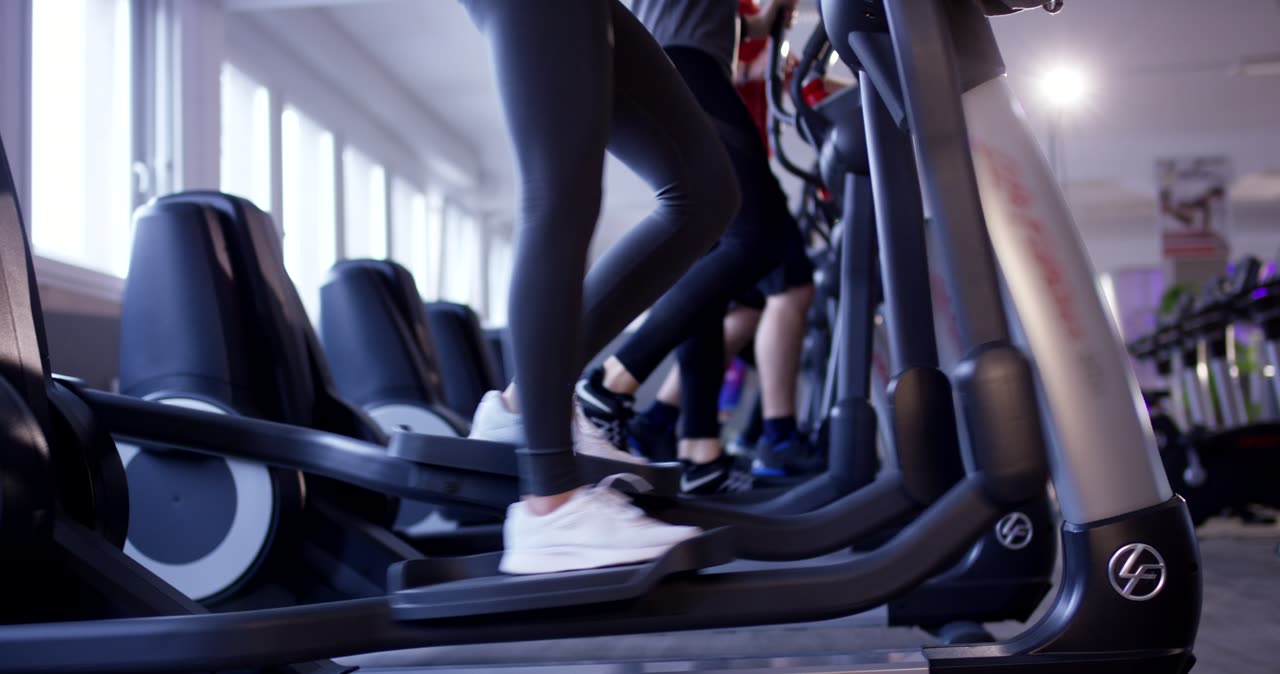 Gruppe von Personen beim synchronen Ausdauertraining auf Crosstrainern im Fitnessstudio