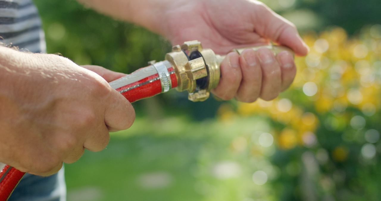 Hände eines Mannes verbinden eine goldene Messing-Schlauchkupplung an einem roten Gartenschlauch im Freien