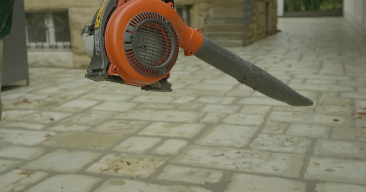 Handwerker bei der Außenreinigung mit einem Laubbläser auf einer gepflasterten TerrasseHandwerker bei der Außenreinigung mit einem Laubbläser auf einer gepflasterten Terrasse