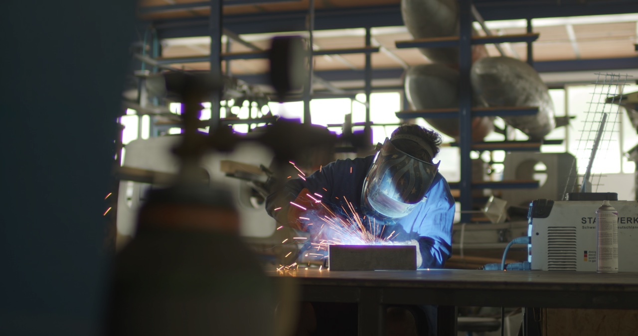 Metallarbeiter mit Schweißschutzmaske beim Schweißen von Bauteilen in einer industriellen Werkstatt