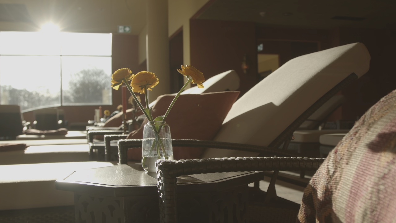 Moderner Ruheraum mit Sonnenliegen und gelben Blumen in einem Spa bei hellem Gegenlicht durch ein großes Fenster