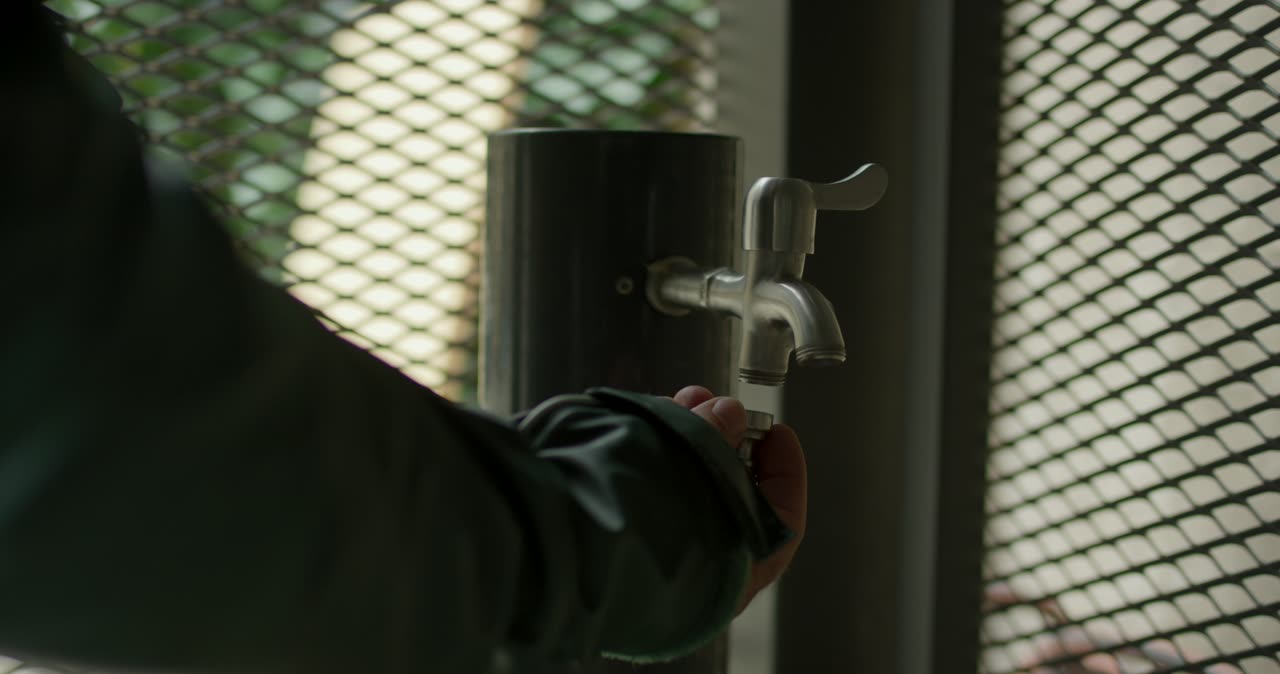 Nahaufnahme von einem Handwerker beim Anschrauben von einem Schlauchanschluss an einen Außenwasserhahn von Hand