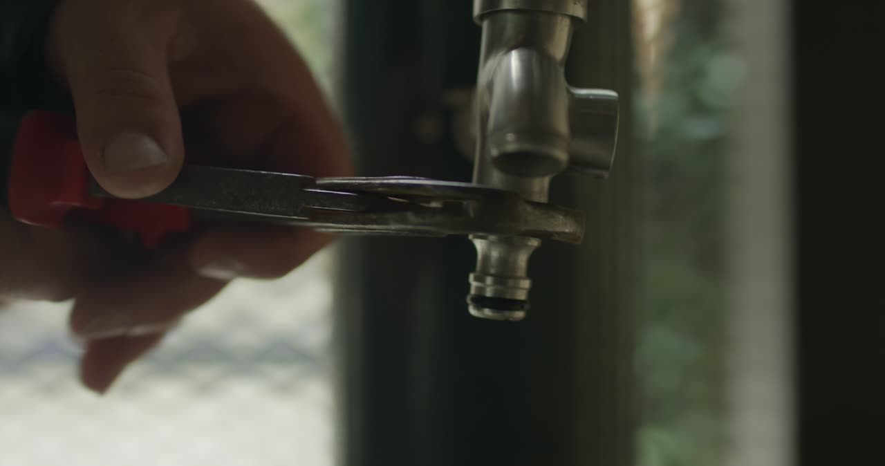 Nahaufnahme von einem Handwerker beim Festziehen oder Lösen von einem Schlauchanschluss am Wasserhahn mit einer Zange