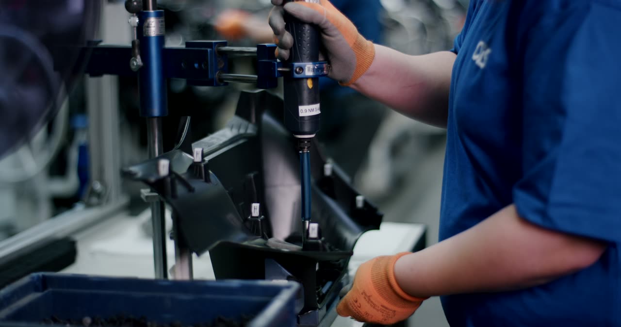 Person verschraubt ein schwarzes Kunststoffbauteil mit einem Elektrowerkzeug in einer Fabrik