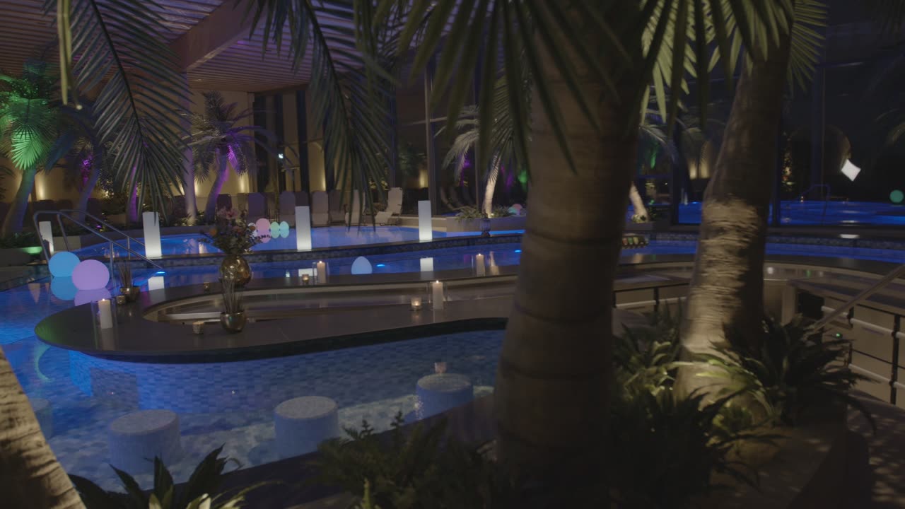 Poolbar in einem nächtlichen Hallenbad mit Palmen und stimmungsvoller Beleuchtung