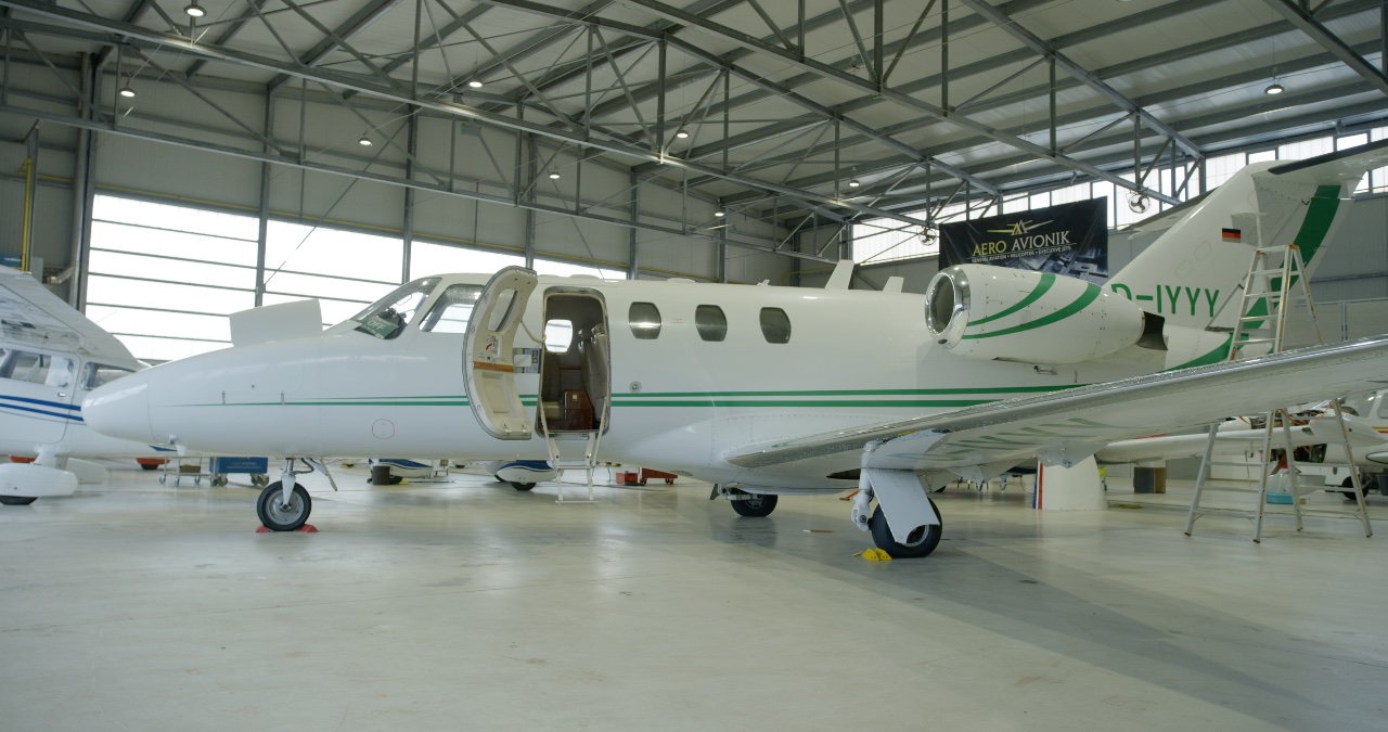 Weißer Privatjet mit grünen Akzenten und geöffneter Kabinentür in einer hellen Flugzeugwartungshalle