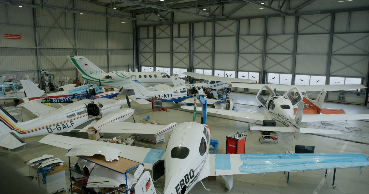 Weitwinkelaufnahme einer Flugzeugwerft mit verschiedenen Kleinflugzeugen und Privatjets während technischer Wartungsarbeiten